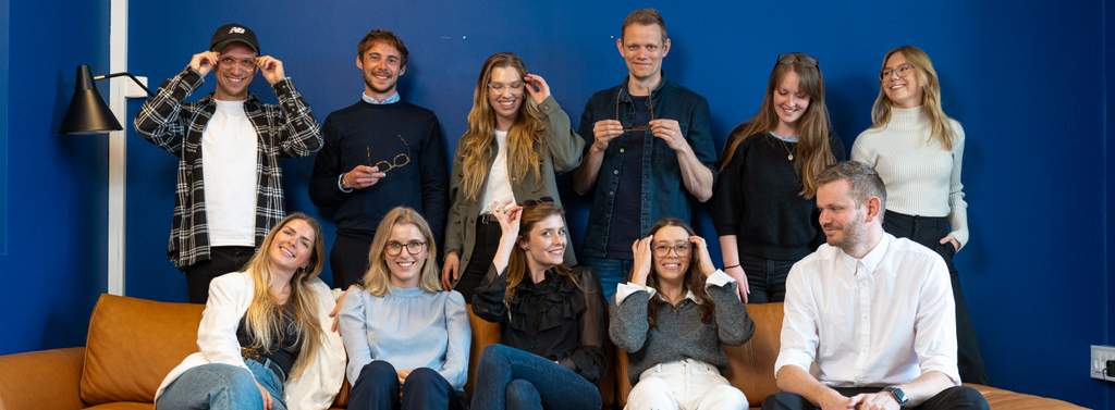 A group of smiling people wearing Luxreaders reading glasses and blue light glasses in front of a blue wall