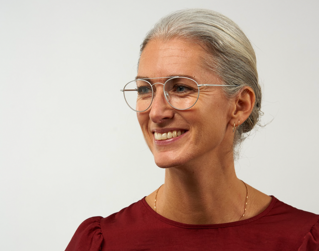 A woman with glasses smiling at the camera, showcasing the perfect glasses for grey hair.